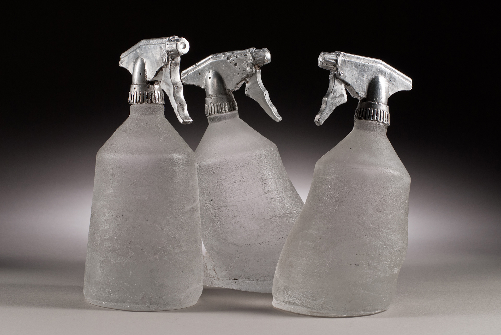 Three cast glass bottles , titled Spray Morped, with printed labels and cast aluminum sprayer nozzles. 